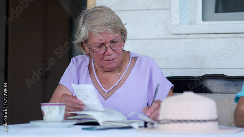 Elderly woman using a pen writing on bank account book while holding the bills to calculate. old lady using calculator, counting savings, taxes.