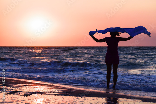 Silhouette of a girl with a blue shawl on the seashore at sunrise  back view