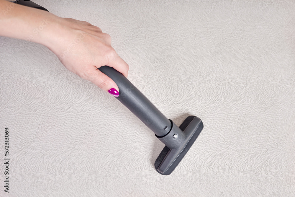 Naklejka premium Close-up of a female hand vacuums the surface of the beige sofa