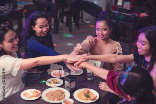 Five young women putting their hands together at the center of the table doing a friendship huddle and making a promise. Workmates piles their hands up each other showing team spirit and unity