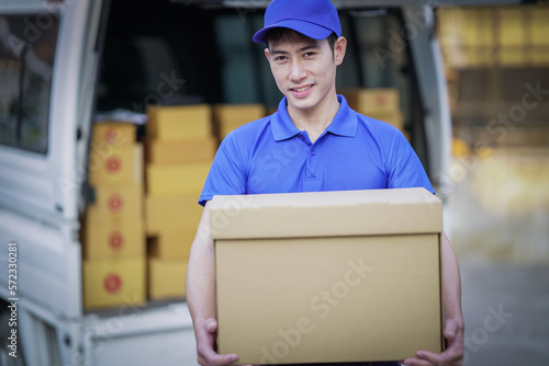 Deliver service. Man With Box in Car Outdoors Delivery Man in uniform holds parcel and phone car outdoors Delivery man taking parcels from The Delivery service. © Tj