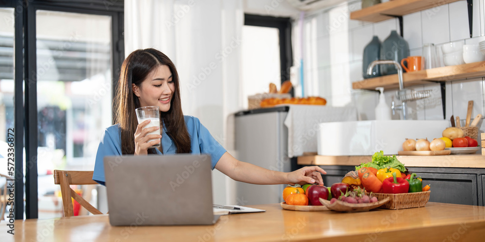Beautiful young asian woman working on laptop computer while sitting at the kitchen room background. Beautiful young asian woman working on laptop computer while sitting at the kitchen room background.