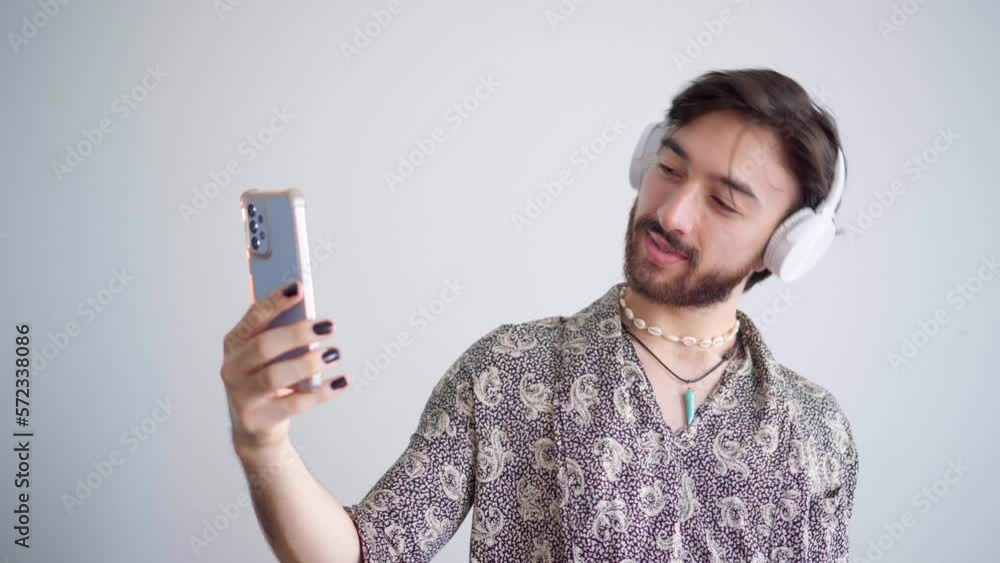 Young queer latin gay man taking pictures of himself with a headphone on a white background. 4k video. Young queer latin gay man taking pictures of himself with a headphone on a white background. 4k video.