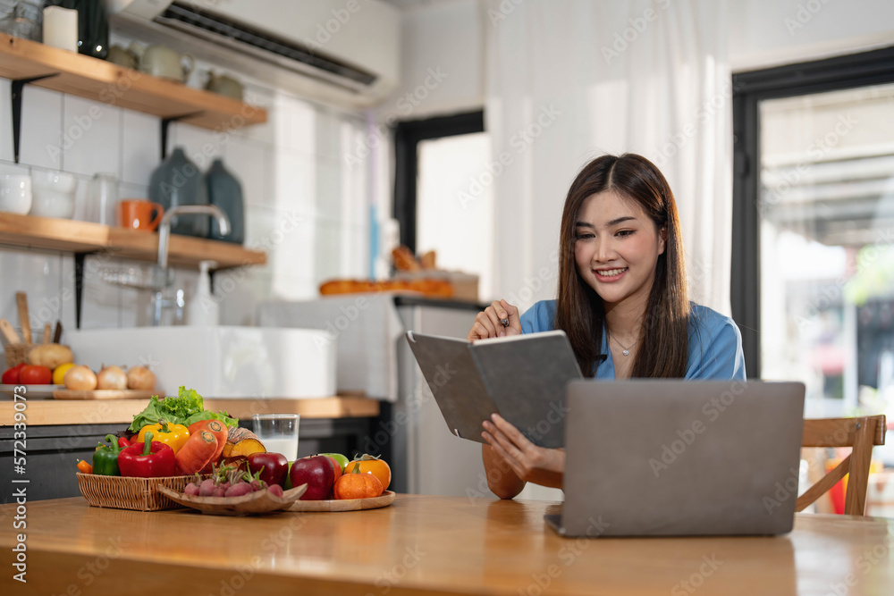 Beautiful young asian woman working on laptop computer while sitting at the kitchen room background. Beautiful young asian woman working on laptop computer while sitting at the kitchen room background.