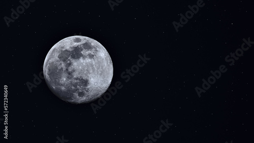 Night Sky. Awe inspiring horizontal left aligned photo of the full moon with visible craters against a star filled black background with copy space.