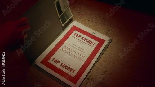 A retro manilla folder containing documents marked 'Top Secret' is seen on a wooden table lit by subdued light.