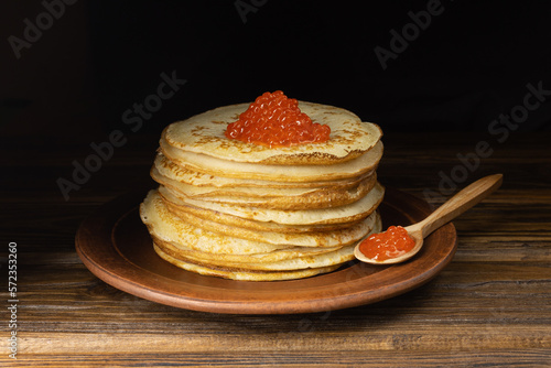 Pancakes with red caviar. A pile of pancakes. Pancakes on a plate and with caviar on a wooden spoon. Red caviar.
