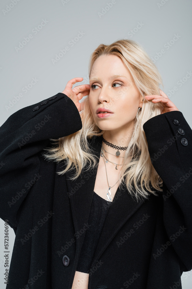 young albino woman adjusting blonde hair and looking away isolated on grey. young albino woman adjusting blonde hair and looking away isolated on grey.