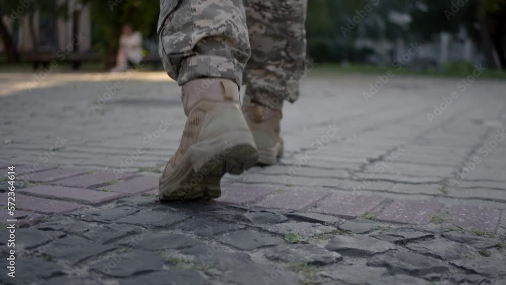 Legs of young man in military uniform walking slowly down the street on a sunny day. Human legs