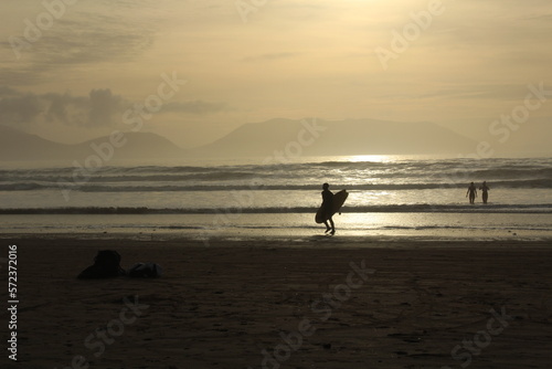 Silhouette of a person surfing at Inch beach at sunset with swimmers in the water (Dingle Peninsula, County Kerry, Ireland).Concept for cold water swimming in winter