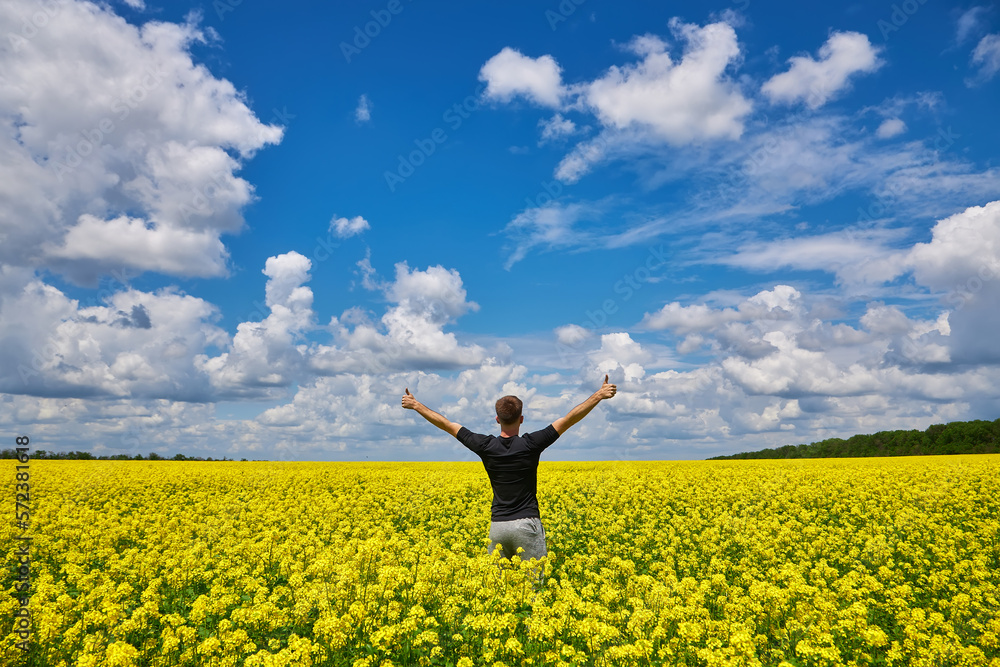 Man with arms outstretched. Handsome young man standing in a field of blooming yellow rapeseed flowers. Man with arms outstretched. Handsome young man standing in a field of blooming yellow rapeseed flowers.
