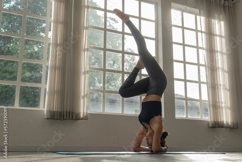 Asian woman practicing yoga standing in headstand at fitness studio