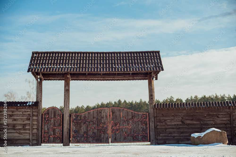 A high wooden fence with wrought iron gates in front of the nature park A high wooden fence with wrought iron gates in front of the nature park