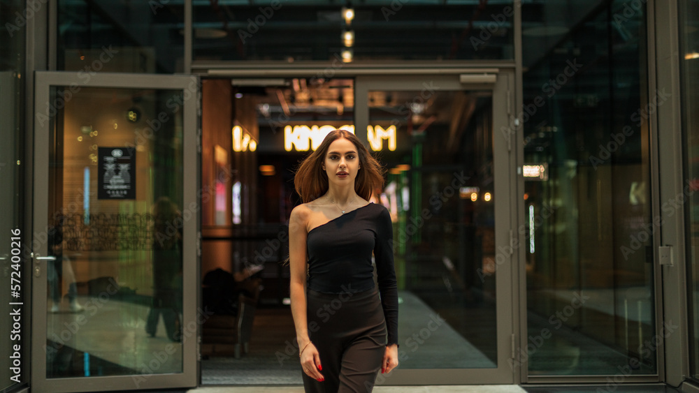 Fashionable beautiful woman model in black stylish clothes with trousers and a black one-shoulder top walks in office building