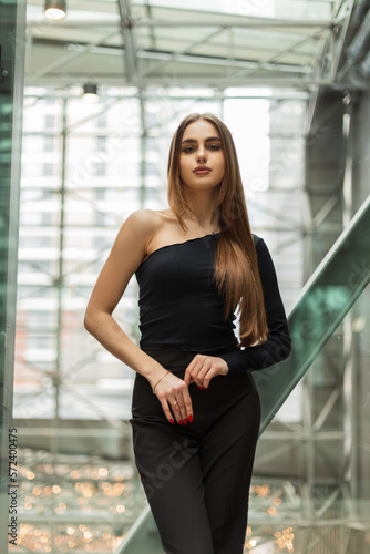 Stylish beautiful woman in fashion black clothes with a one-shoulder top and trousers in an office building. office manager lady