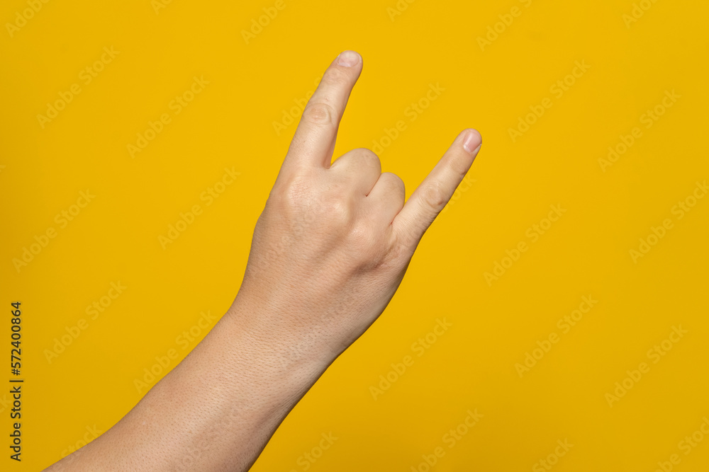 Naklejka premium Male hand close-up on a yellow background shows hand gesture. Rock'n'roll. Isolate
