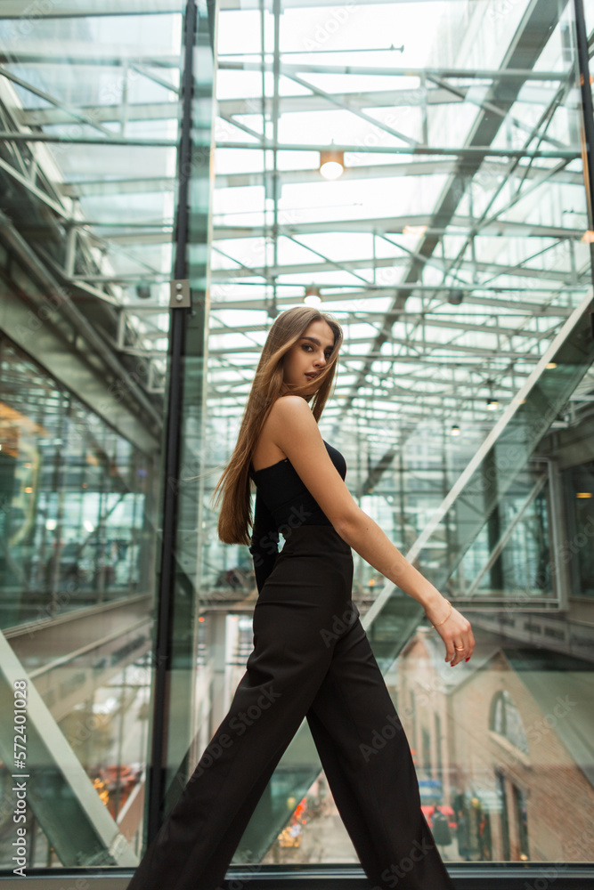Stylish beautiful successful business woman model in fashion black elegant clothes with a top and pants walking in a glass office building Stylish beautiful successful business woman model in fashion black elegant clothes with a top and pants walking in a glass office building
