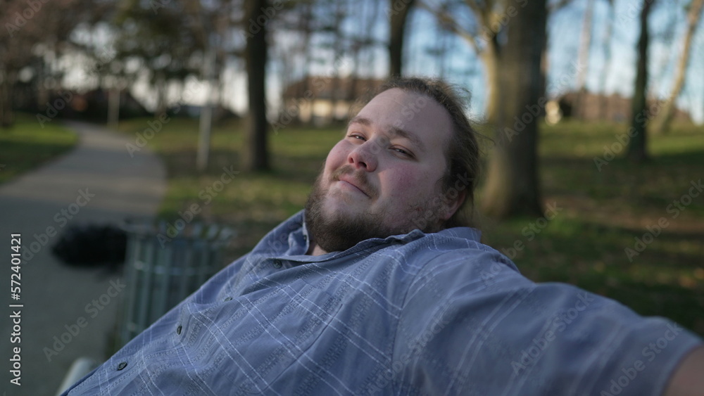 Portrait of a happy overweight man sitting at park bench looking at camera smiling during sunset Portrait of a happy overweight man sitting at park bench looking at camera smiling during sunset