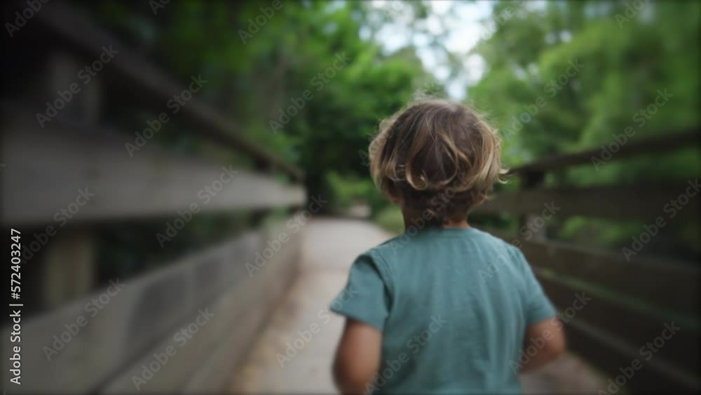Back of carefree little boy running in wooden bridge nestled in beautiful greenery forest. Happiness concept of child runner Back of carefree little boy running in wooden bridge nestled in beautiful greenery forest. Happiness concept of child runner