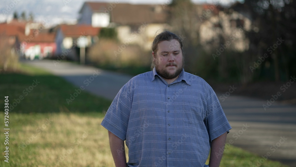 One young thoughtful chubby man standing outdoors thinking. Pensive expression of an overweight male person in contemplation. A meditative individual One young thoughtful chubby man standing outdoors thinking. Pensive expression of an overweight male person in contemplation. A meditative individual