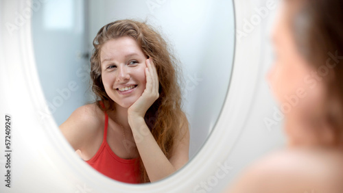 Anxious young woman look in the mirror worried about wrinkle or acne on unhealthy skin  upset unhappy millennial female examine squeeze pimple on face in the bedroom  cosmetology  skincare concept 