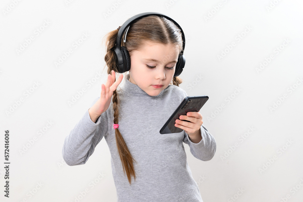 A girl with headphones and a phone on a white background, a girl with pigtails listens to music in headphones, photo with copy space. A girl with headphones and a phone on a white background, a girl with pigtails listens to music in headphones, photo with copy space.