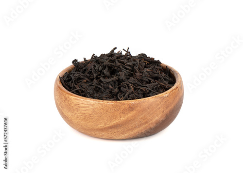 Dry black tea leaves in a wooden bowl over white background.