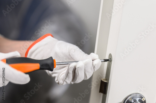 men's hands with a manual screwdriver and a screw handle on a white door. Door lock attachment.