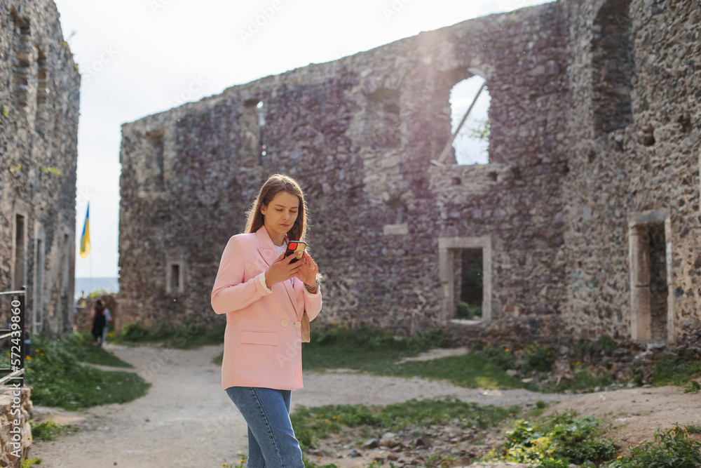 A girl is holding a phone in the middle of a ruined medieval castle