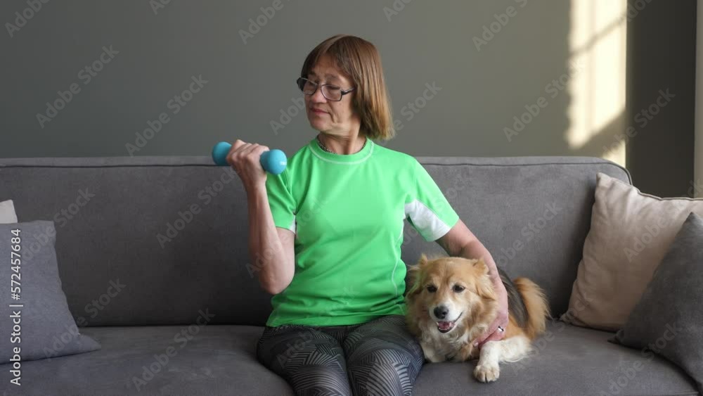 Active senior does sports at home on a gym mat, his beloved dog watches next to him on the sofa. The concept of peace of mind and tranquility. Active senior does sports at home on a gym mat, his beloved dog watches next to him on the sofa. The concept of peace of mind and tranquility.