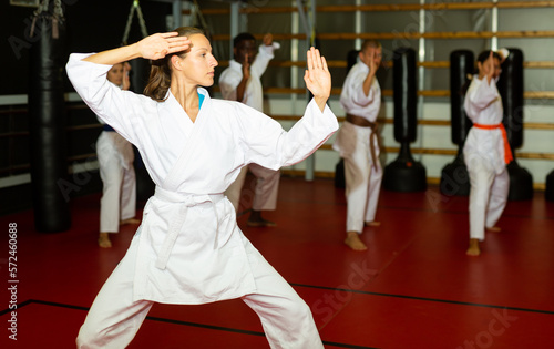 European woman posing in front of camera and showing fight stance during group karate training.