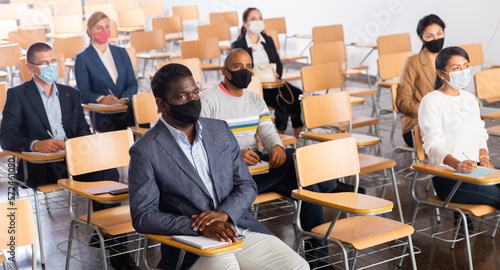 International group of business people wearing protective face masks listening to presentation in conference room. Concept of precautions and social distancing in COVID 19 pandemic