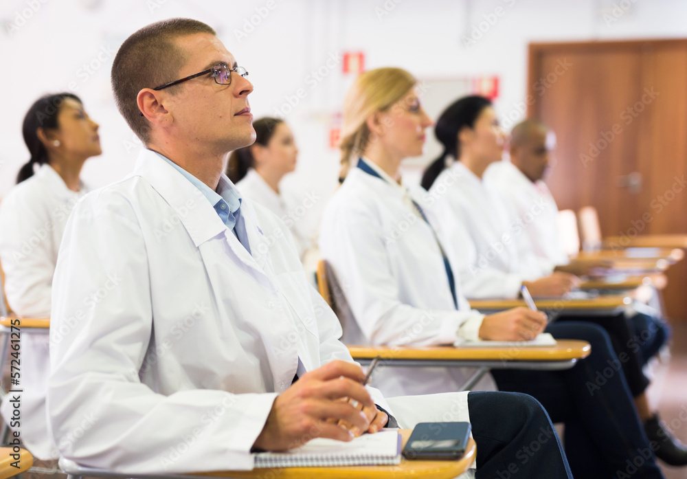 Fototapeta premium Portrait of male doctor attentively listening to lecture with colleagues at medical conference