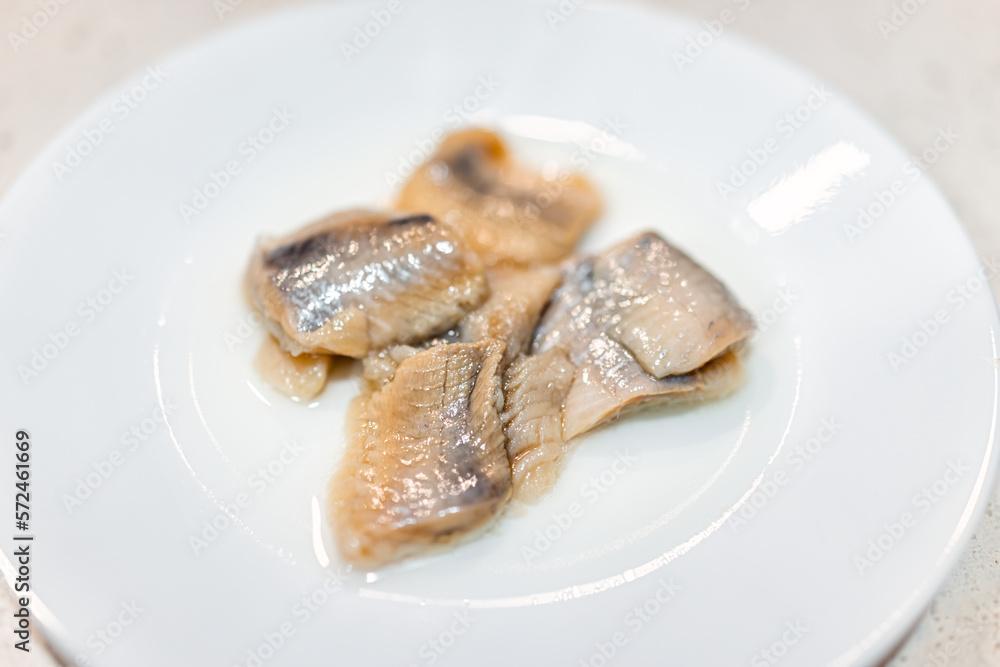 Pickled wild caught herring pieces macro closeup with texture of fillets on white plate studio shot as traditional Eastern European food