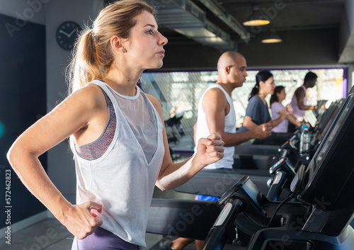 Slender athletic positive european girls running on treadmill in fitness club
