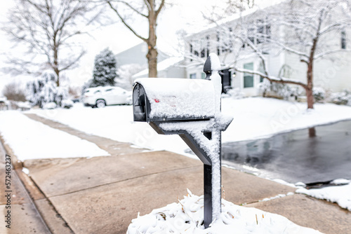 White snow covered mailbox on sidewalk street in northern Virginia suburbs and single family house in Washington DC metro area in winter season weather