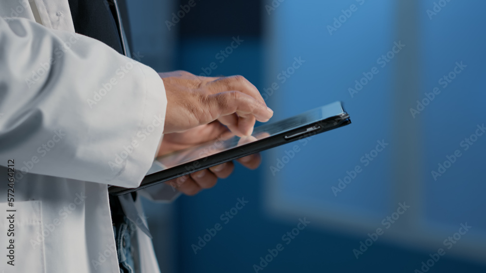 Close up of general practitioner holding tablet computer searching for patient disease report before start planning medication treatment in hospital office. Medical team working night shift