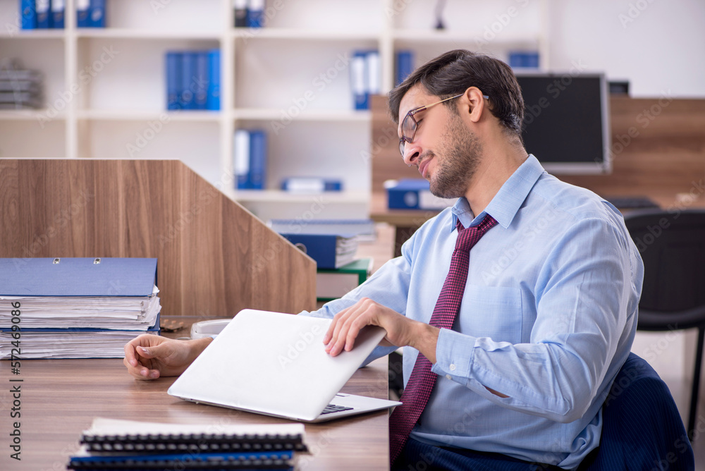 Young male employee unhappy with excessive work at workplace Young male employee unhappy with excessive work at workplace