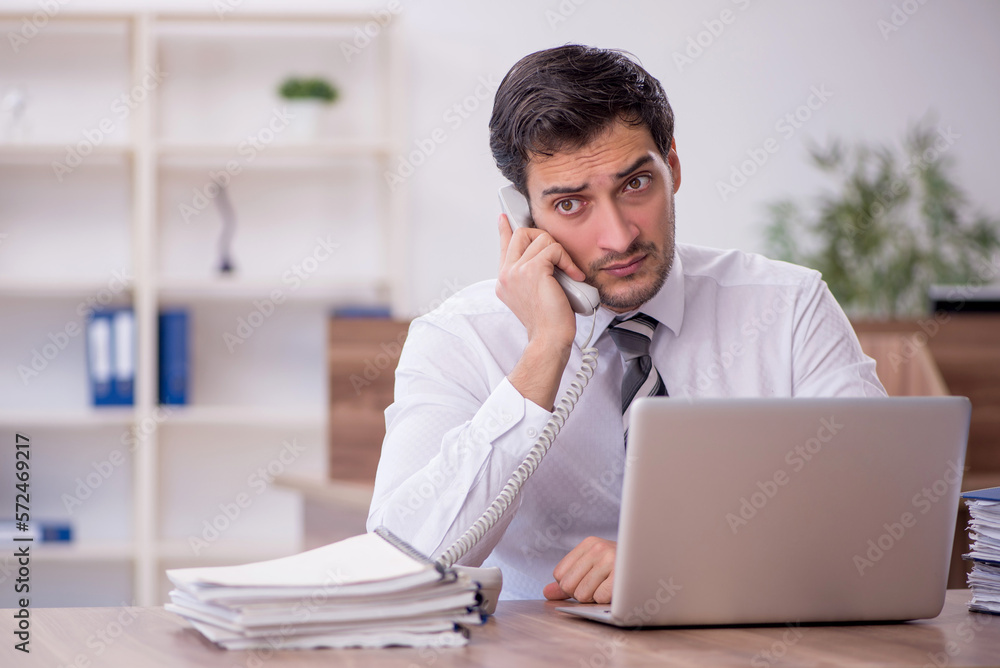 Young male employee unhappy with excessive work at workplace Young male employee unhappy with excessive work at workplace