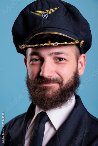 Aircraft captain wearing uniform and hat portrait, confident plane pilot standing with crossed arms, looking at camera. Smiling civil aviator with badge on professional suit © DC Studio