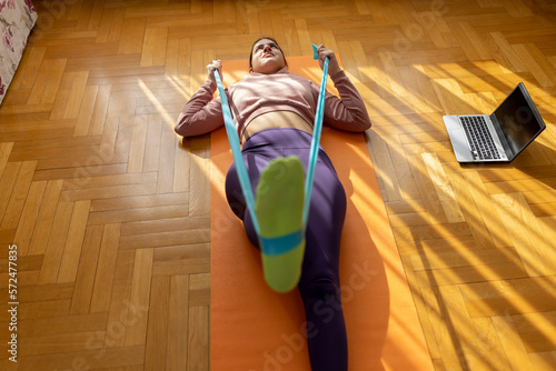 Online workout. Teen girl doing Sport exercise at home, watching tutorials on a laptop. How to keep fit indoors