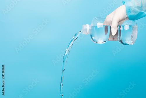Saline medical cleaning normal solution plastic bottle in hand of nurse with glove, pouring water of normal saline in plastic bottle to clean sterile medical equipment over blue background isolated
