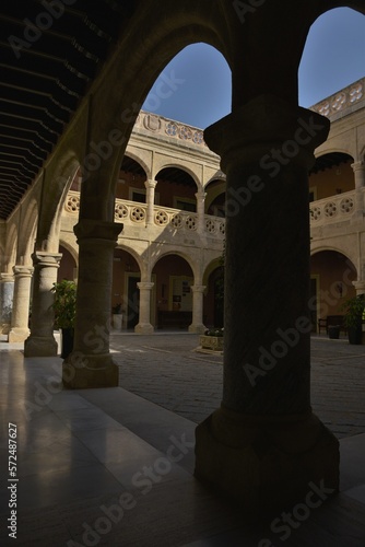 Shadow and light between the elegant arches of the two storey courtyard of Castillo de Luna fortress lined by beautiful round Gothic roses in bright yellow sandstone, Rota, Spain
