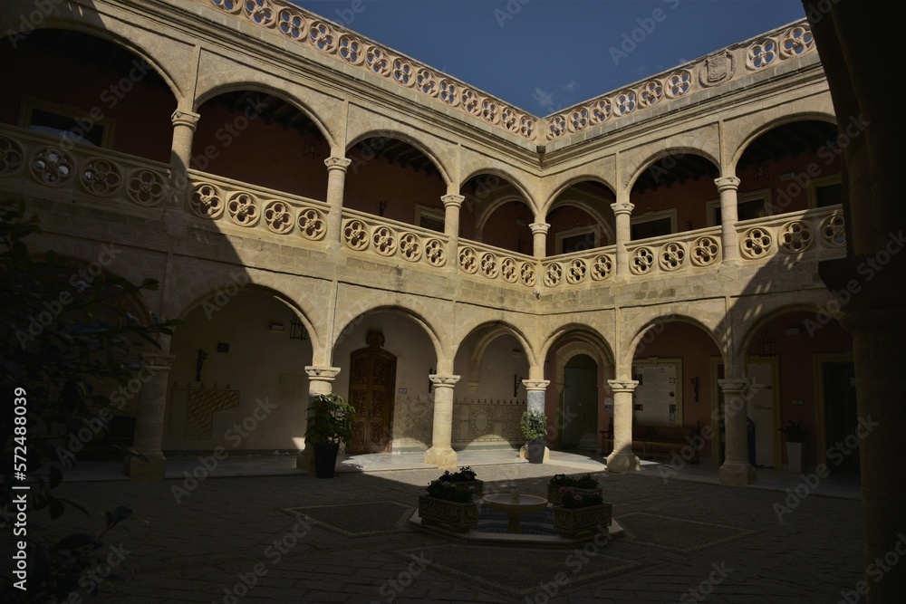 Elegant arches of the two storey courtyard of Castillo de Luna fortress lined by two rows of beautiful round Gothic roses in yellow sandstone, small fountain in the center, Rota, Spain