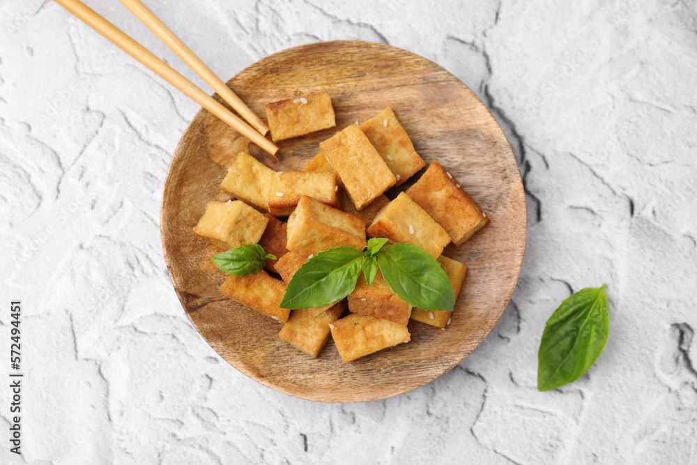 Wooden plate with delicious fried tofu, basil and sesame seeds on light grey table, top view Wooden plate with delicious fried tofu, basil and sesame seeds on light grey table, top view