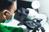 Scientist Looking Under Microscope, Wearing Green Protective Clothing. Hospital Medical Development Laboratory. Medicine, Biotechnology, Microbiology, and Drugs