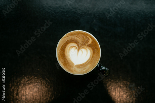 A Hot Coffee Latte with Artistic Heart Shape on a Black Table at a Coffee Shop.
