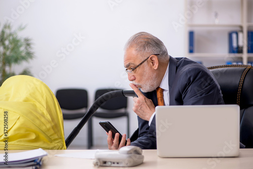 Old male employee looking after new born at workplace