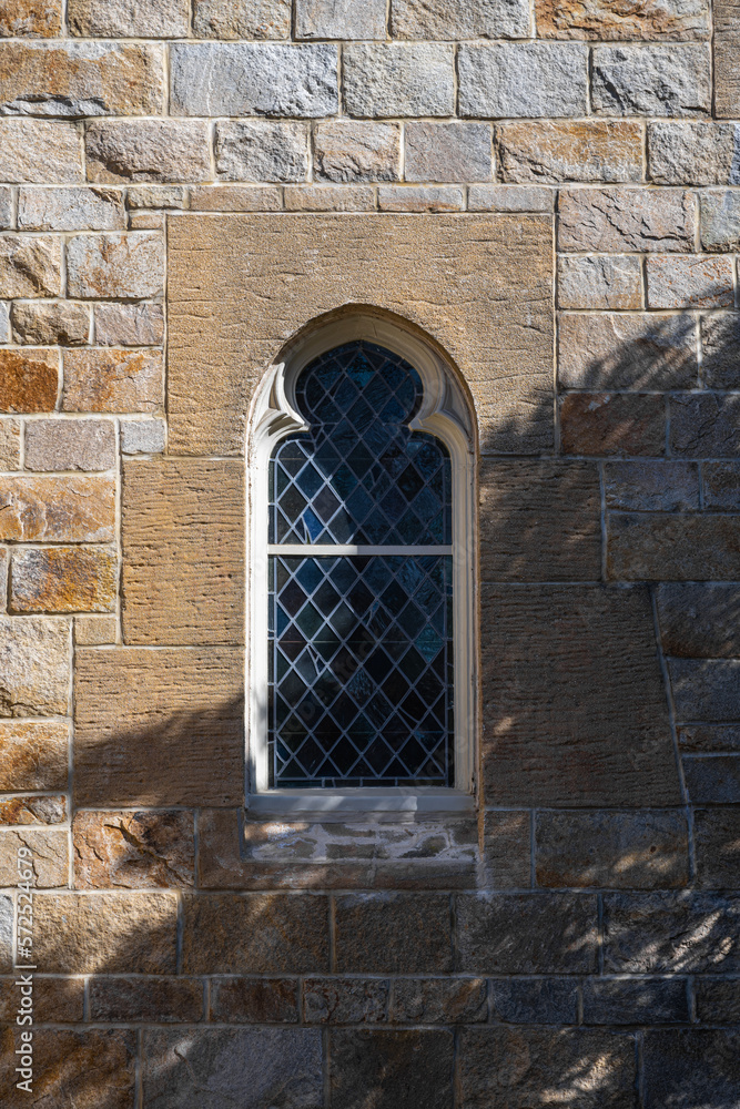 window in the stone wall of the church with shadow of trees