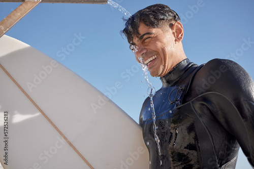 Slika na platnu Man, surfing and water shower at beach on face, smile or blue sky in summer, sunshine or ocean travel